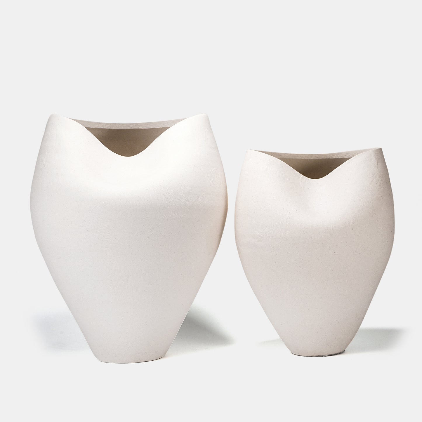 This pair of large ceramic vases captivates with organic ocean-inspired curves and a sandy matte white finish. Designed as tall floor vases, stage them symmetrically with cascading flowers on vase displays or dried pampas grass, while clustering bud vases at their base for textural contrast. Their neutral white color vase aesthetic harmonizes with coastal and modern interiors. 