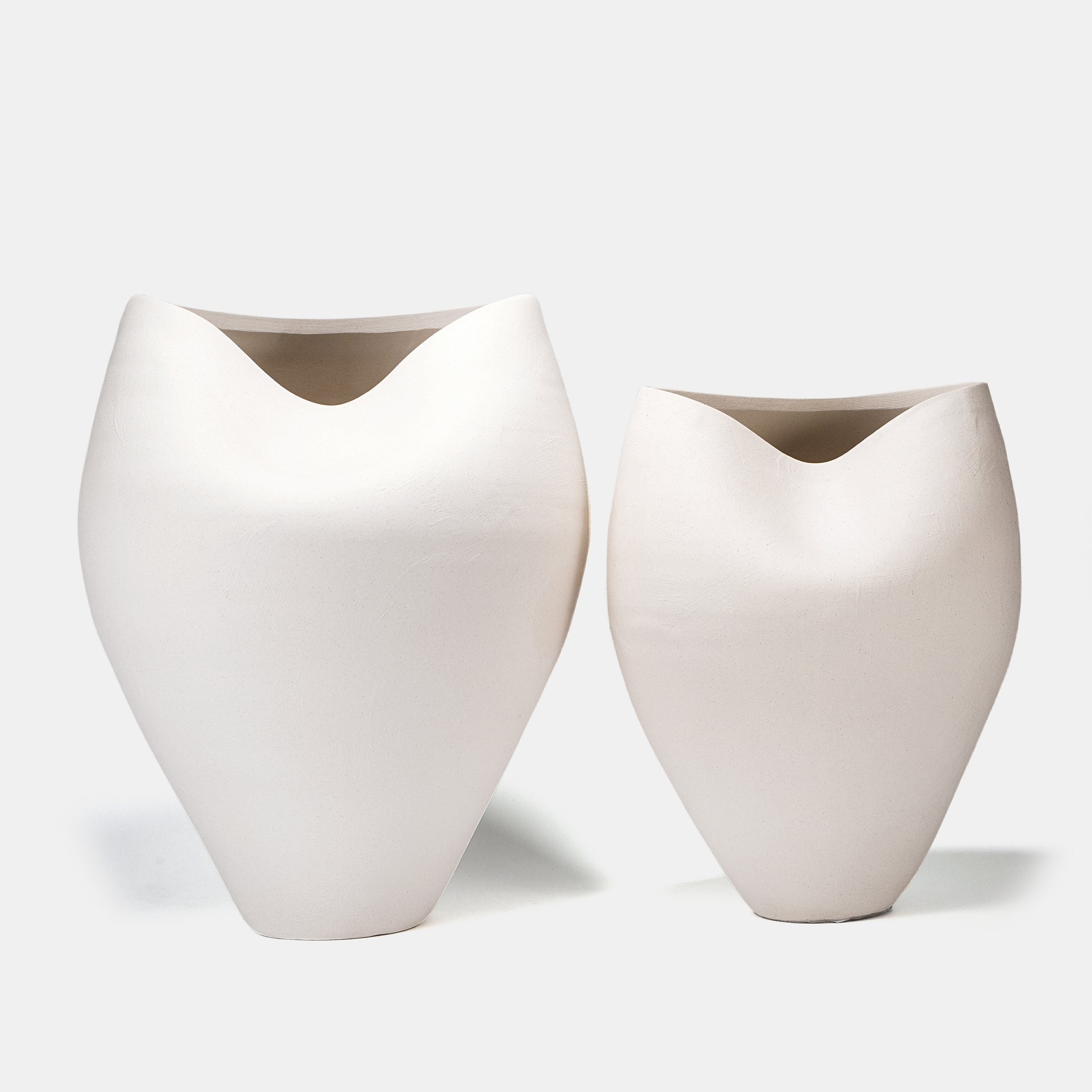 This pair of large ceramic vases captivates with organic ocean-inspired curves and a sandy matte white finish. Designed as tall floor vases, stage them symmetrically with cascading flowers on vase displays or dried pampas grass, while clustering bud vases at their base for textural contrast. Their neutral white color vase aesthetic harmonizes with coastal and modern interiors. 